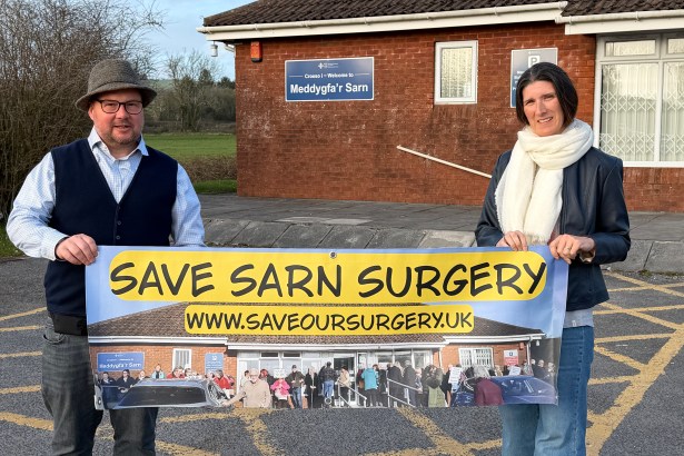 Carl Peters-Bond with Meddygfa'r Sarn campaign organiser, Clare Treharne in front of the surgery holding a protest banner
